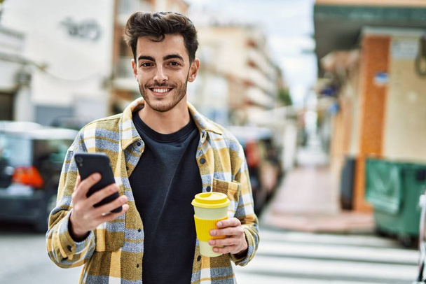 Fešák hispánec muž usmívá šťastný a jistý ve městě pomocí smartphonu - Fotografie, Obrázek