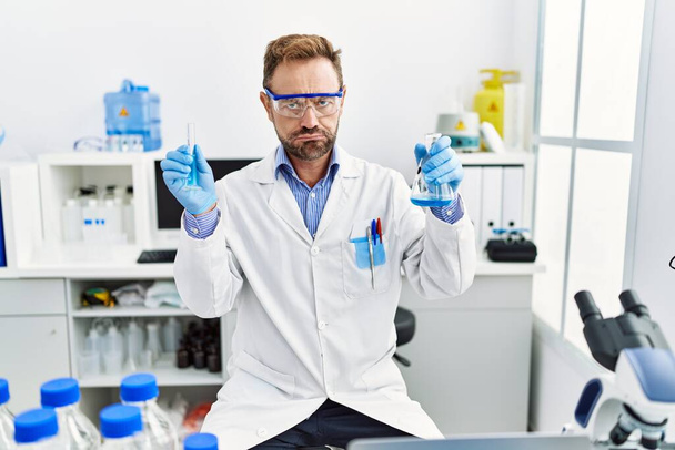 Középkorú férfi dolgozik tudós laboratórium kezében kémiai termékek depressziós és aggódni a szorongás, sír dühös és fél. szomorú kifejezés.  - Fotó, kép