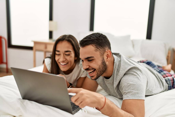 Fiatal latin pár mosolyog boldog segítségével laptop fekszik az ágyon. - Fotó, kép