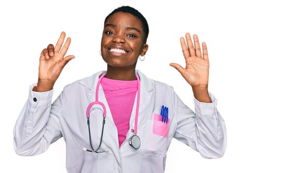 Genç Afro-Amerikan kadın doktor üniforması ve steteskop giyiyor. Sekiz numarayı gösterip işaret ederken kendinden emin ve mutlu gülümsüyor..  - Fotoğraf, Görsel