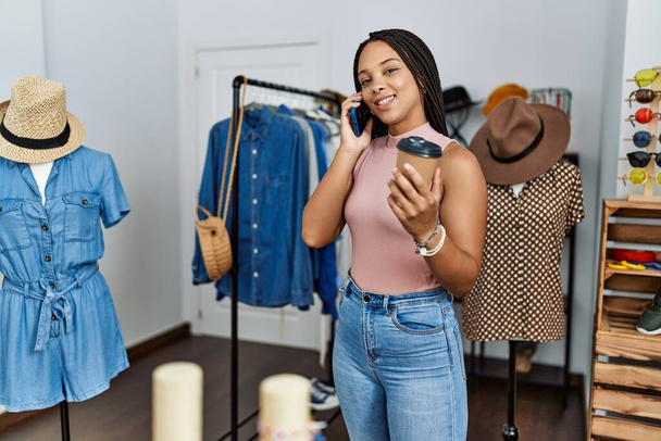 Genç Afro-Amerikalı kadın akıllı telefondan konuşuyor. Giyim mağazasında kahve içiyor. - Fotoğraf, Görsel