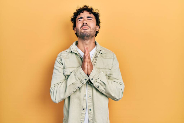 Jeune homme hispanique portant des vêtements décontractés mendier et prier avec les mains ainsi que l'expression de l'espoir sur le visage très émotionnel et inquiet. mendier.  - Photo, image