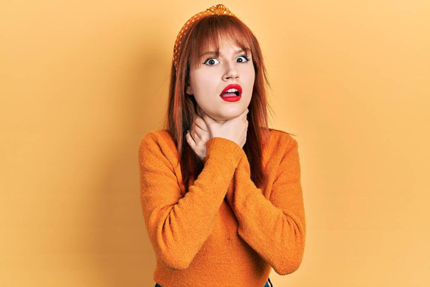 Κοκκινομάλλα νεαρή γυναίκα που φοράει πορτοκαλί πουλόβερ φωνάζοντας και ασφυκτιώντας από οδυνηρό στραγγαλισμό. πρόβλημα υγείας. ασφυξία και έννοια της αυτοκτονίας.  - Φωτογραφία, εικόνα
