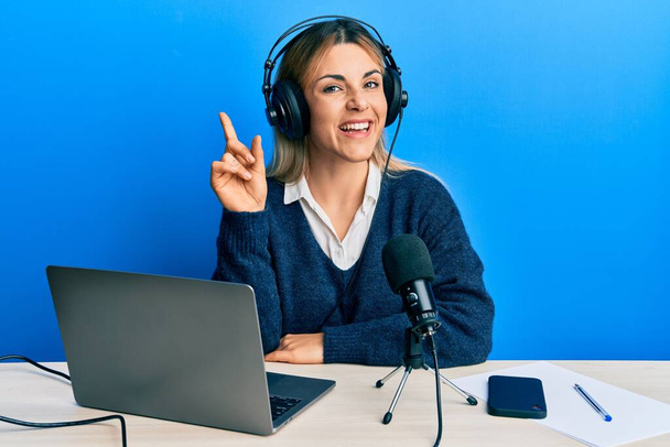 Jeune femme caucasienne travaillant au studio de radio souriant avec une idée ou une question pointant du doigt avec le visage heureux, numéro un  - Photo, image