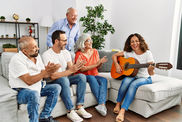 Gruppo di amici di mezza età che fanno festa suonando la chitarra classica seduti sul divano a casa. - Foto, immagini