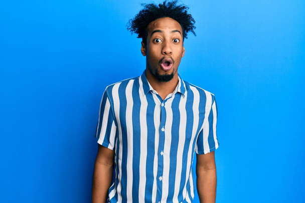 Νεαρός Αφροαμερικάνος με γενειάδα φορώντας ριγέ πουκάμισο φοβισμένος και σοκαρισμένος από την έκφραση έκπληξη, το φόβο και το ενθουσιασμένο πρόσωπο.  - Φωτογραφία, εικόνα