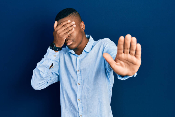 Junger afrikanisch-amerikanischer Mann in lässiger Kleidung, der die Augen mit Händen bedeckt und mit traurigem und ängstlichem Gesichtsausdruck Stopp-Gesten macht. Peinliches und negatives Konzept.  - Foto, Bild