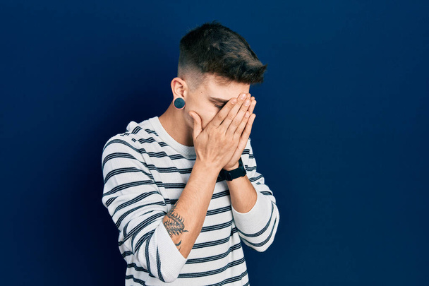 Young caucasian boy with ears dilation wearing casual striped shirt with sad expression covering face with hands while crying. depression concept.  - Photo, Image