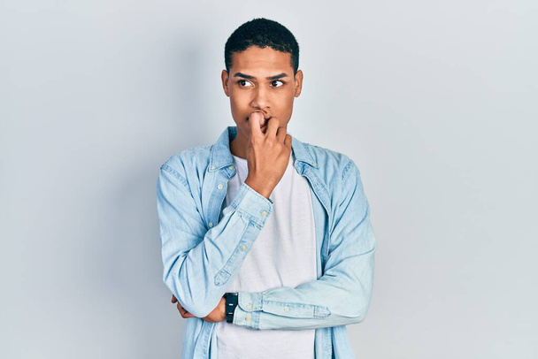 Joven afroamericano tipo usando ropa casual buscando estresado y nervioso con las manos en la boca mordiendo las uñas. problema de ansiedad.  - Foto, imagen