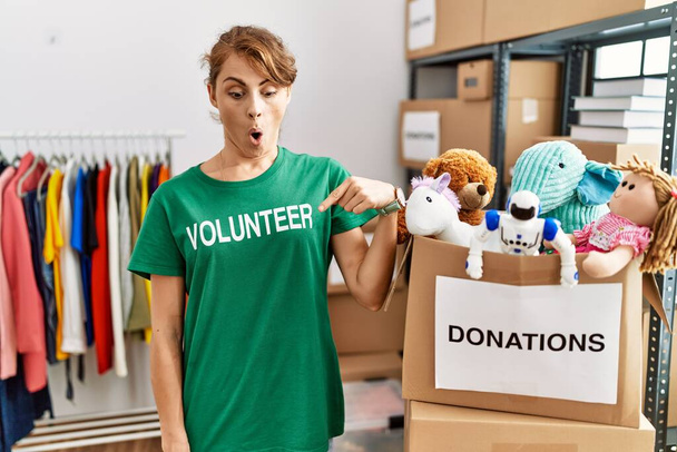 Mulher branca bonita vestindo t-shirt voluntária em doações stand apontando para baixo com os dedos mostrando propaganda, rosto surpreso e boca aberta  - Foto, Imagem