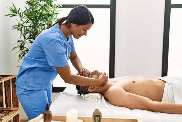 Jovem massagem latina terapeuta mulher dando tratamento relaxante na cabeça do homem no centro de beleza. - Foto, Imagem