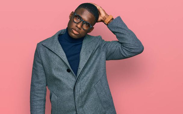 Young african american man wearing business clothes and glasses confuse and wondering about question. uncertain with doubt, thinking with hand on head. pensive concept.  - Photo, Image