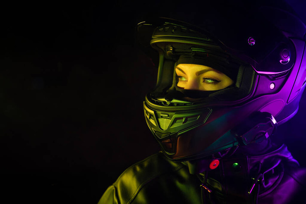 Portrait of confident motorcyclist woman in closed motorcycle helmet. Young driver biker under colorful neon light at night. Copy space. - Фото, зображення