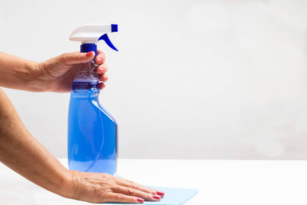 Hands hold bottle of blue liquid spray and sponge on table. Copy space. Cleaning products. White background. - Φωτογραφία, εικόνα