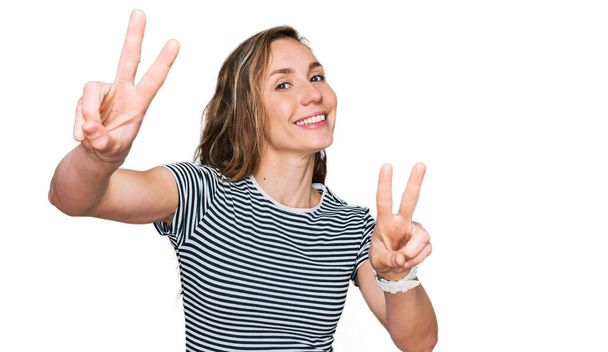 Young blonde woman wearing casual clothes smiling looking to the camera showing fingers doing victory sign. number two.  - Photo, Image