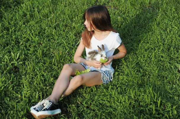 Una niña alimenta a un conejo con hojas de col al aire libre. El conejo como símbolo de la Pascua. Buen trato del niño con el animal.  - Foto, imagen