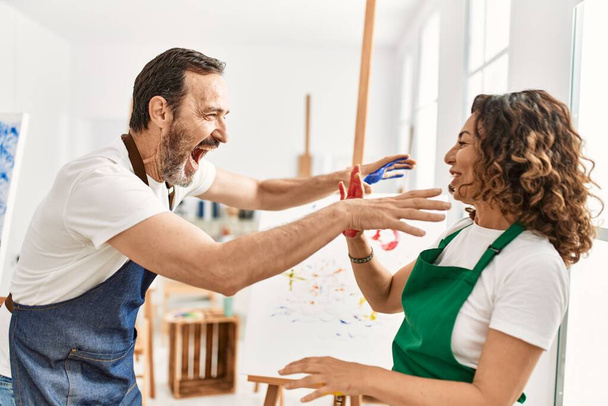 Due studenti di mezza età sorridenti felici giocando con le mani di vernice in studio d'arte. - Foto, immagini