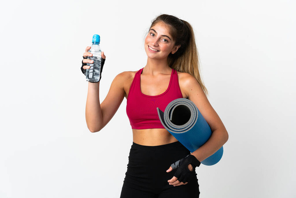 Young caucasian woman isolated on white background with sports water bottle and with a mat - Foto, Imagen