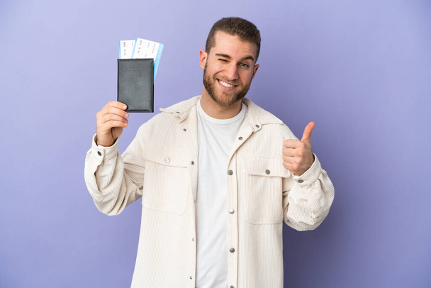 Young handsome caucasian man isolated on purple background in vacation holding a passport and plane with thumb up - Foto, afbeelding
