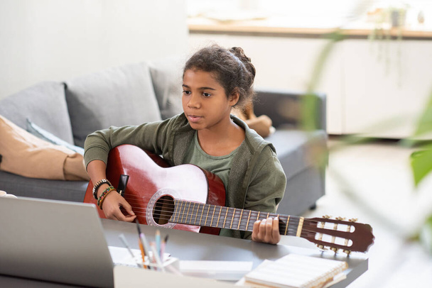 Dizüstü bilgisayarının önünde gitar çalan ciddi bir kız öğrenci. - Fotoğraf, Görsel