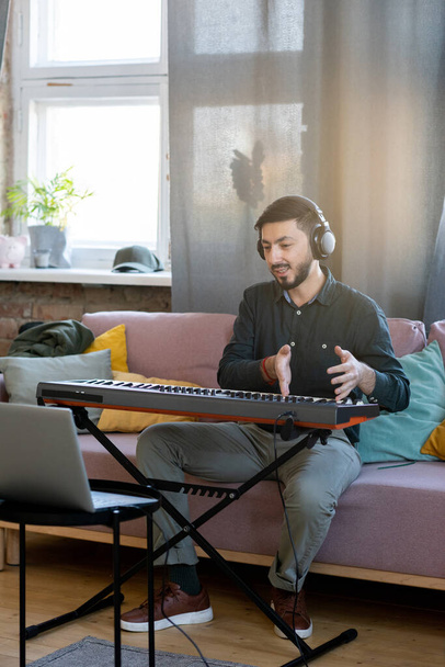 Молодий чоловік в навушниках пояснює правила гри на клавіатурі піаніно
 - Фото, зображення