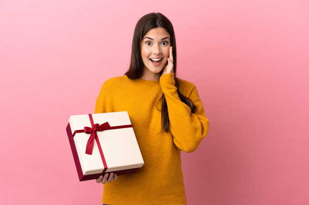 Teenager ragazza brasiliana in possesso di un regalo su isolato sfondo rosa con sorpresa e scioccato espressione facciale - Foto, immagini
