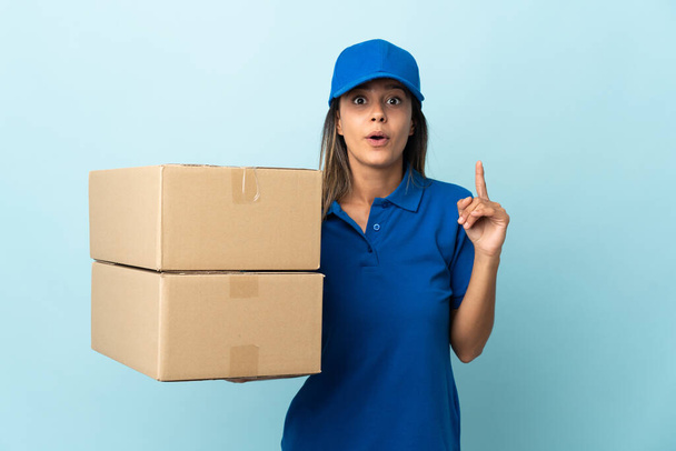 Jonge levering vrouw geïsoleerd op blauwe achtergrond van plan om de oplossing te realiseren, terwijl het opheffen van een vinger omhoog - Foto, afbeelding