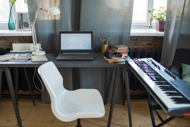 Белый стул между столом с ноутбуком и клавиатурой фортепиано - Фото, изображение
