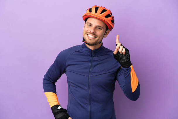 Fiatal brazil kerékpáros férfi elszigetelt lila háttér mutatja és emeli az ujját a jel a legjobb - Fotó, kép