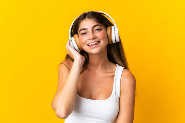 Молодая белая женщина, изолированная на желтом фоне, слушает музыку - Фото, изображение