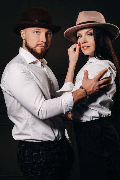 A man and a woman in white shirts and hats on a black background.A couple in love poses in the interior of the studio. - Foto, immagini