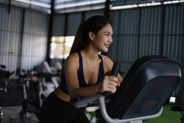 Glückliche junge Frau lächelt und trainiert mit Sport-Fahrrad-Fitness im Kurs gegen Fitness-Schnittstelle - Foto, Bild