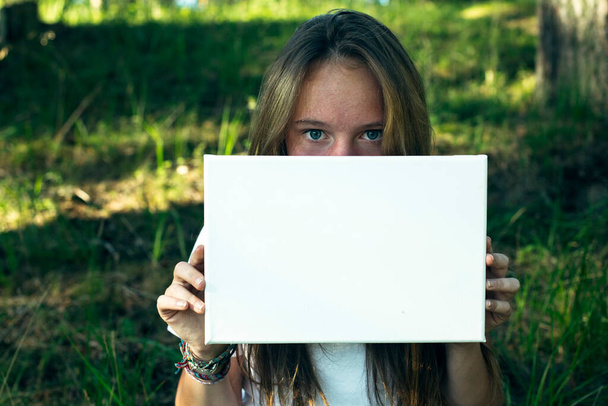 緑の公園できれいな白い紙(メッセージのためのバナー)を持っている女の子のクローズアップ. - 写真・画像