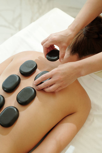 Hands of masseuse putting hot spa stones on female back - Foto, Bild