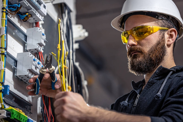 um eletricista masculino trabalha em um quadro com um cabo de conexão elétrica
. - Foto, Imagem