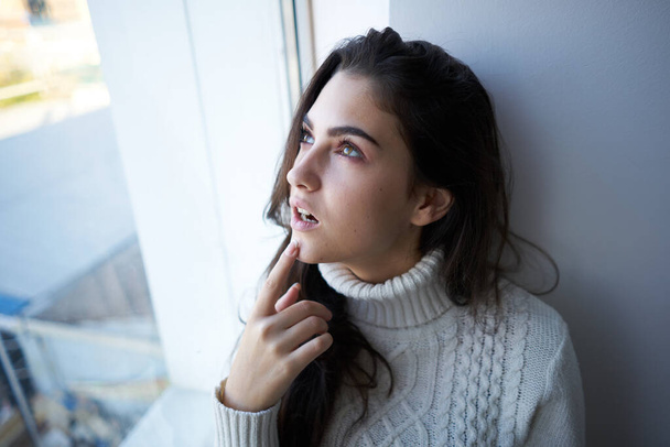 brunette in a white sweater looks out the window depression - Foto, immagini
