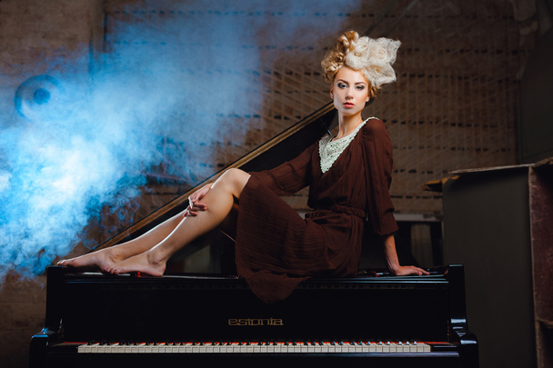 Chica en un vestido marrón permanecer en el piano
 - Foto, imagen