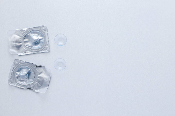 Two contact lenses in a closed package and two open contact lenses lie on the side on a white background with space for text. top view, flat lay, copy space, isolate - Foto, Bild