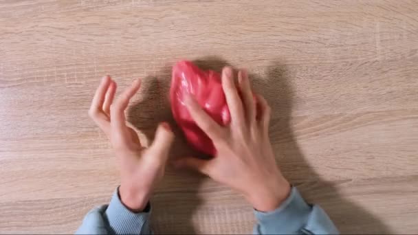 Spiel mit Schleim, Stretching der gooey Substanz für Spaß und Stressabbau. Nahaufnahme und Draufsicht der weiblichen Hand, die roten, glänzenden Schleim hält und ihn zusammendrückt. Video in 4K-Auflösung - Filmmaterial, Video