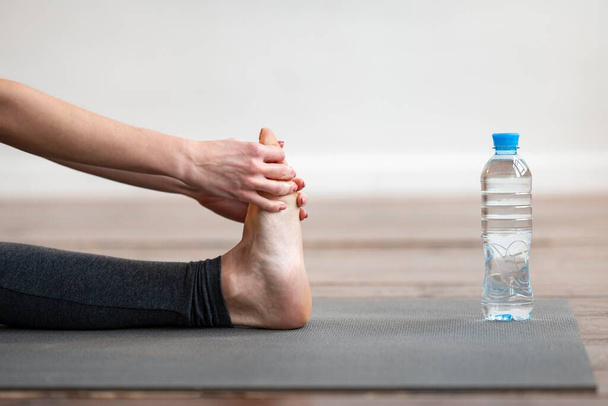 vista lateral mujer estiramiento yoga estera con botella de agua. Foto de alta calidad - Foto, Imagen
