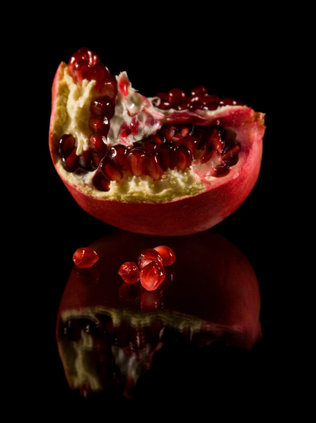 Pomegranate; broken fruit isolated on black reflective surface; - Valokuva, kuva