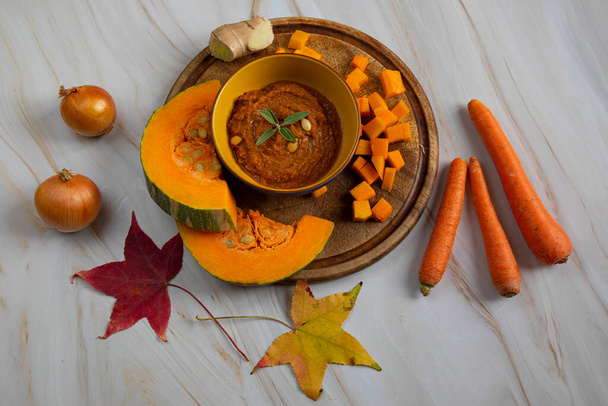 Осінні страви, приготування гарбузового супу. гарбуз на дерев'яній дошці, поруч з цибулею, морквою та імбиром
 - Фото, зображення
