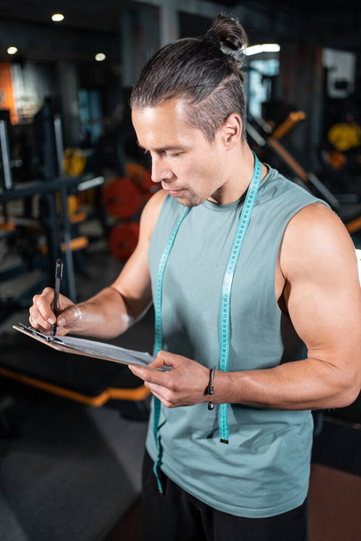 young attractive man personal trainer planning workout with clipboard in gym - Fotografie, Obrázek