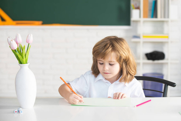 Pupil doing lessons at home. School kid writing something in copybook and sitting at table in classroom. First grader. - Foto, imagen