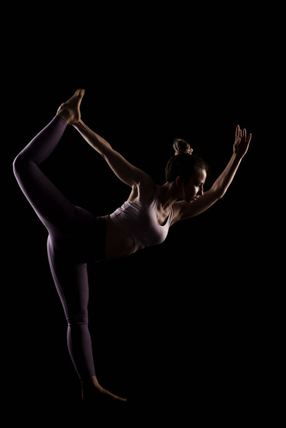 Fit girl practicing yoga in a studio. Half silhouette side lit fitness model - Fotografie, Obrázek