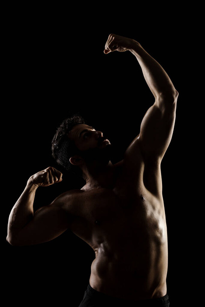 Side lit muscular Caucasian man silhouette. Athlete posing against black background.  - Фото, зображення