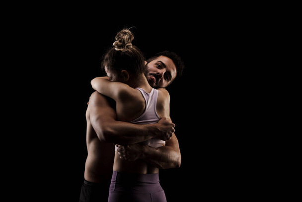 Fit couple in love hugging together. Boy and girl side lit on black background. - Фото, зображення