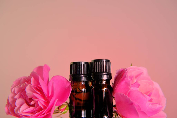 Rose eteerinen öljy.Aromaterapia ja kosmetiikka. Lasipullot asetettu ja vaaleanpunainen ruusu kukkia vaaleanpunainen taustalla.Organic luonnollinen ruusu öljyä.Organic bio kosmetiikka - Valokuva, kuva