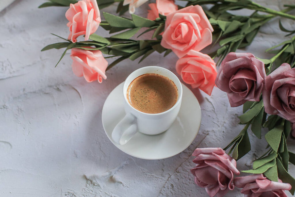 Šálek kávy s růžovou květinou na bílém stole pozadí. Valentýn s místem pro text. Klasická fotka. Mezera pro text - Fotografie, Obrázek