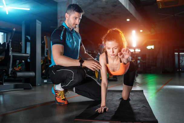 young woman exercising quadruplex with personal trainer in gym - Φωτογραφία, εικόνα